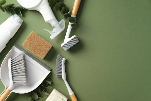 Cleaning supplies on a green background, including brushes, a dustpan, sponges, and spray bottles. Perfect for illustrating household cleaning themes.