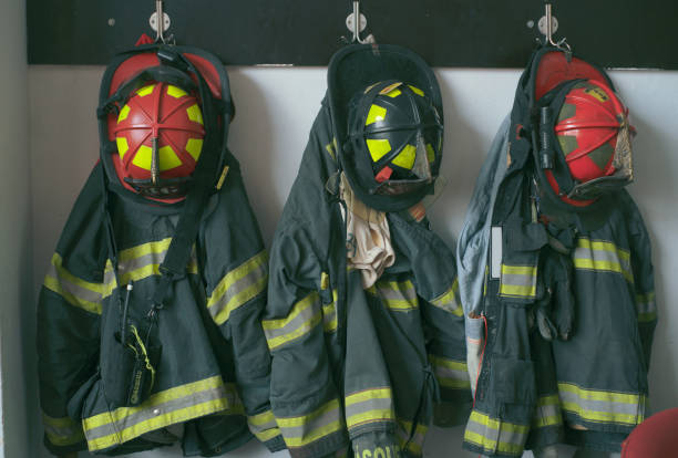 Firefighter uniforms and helmets hanging on a wall in a fire station Firefighter uniforms and helmets hanging on a wall in a fire station